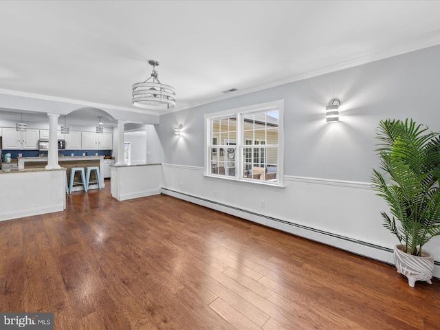 unfurnished living room with a baseboard heating unit, dark wood-style flooring, crown molding, visible vents, and ornate columns