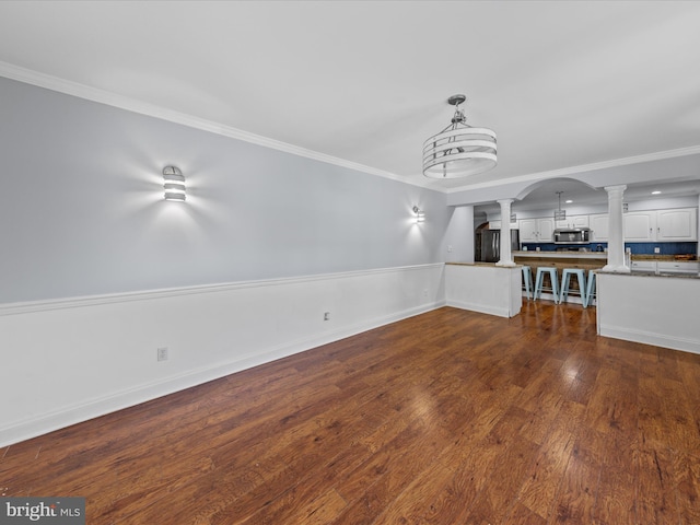 unfurnished living room with crown molding, dark wood finished floors, arched walkways, and ornate columns