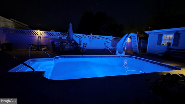 pool at night with a water slide, fence, a fenced in pool, and a patio area