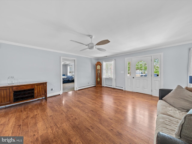 living room with wood finished floors, baseboard heating, ceiling fan, baseboards, and crown molding