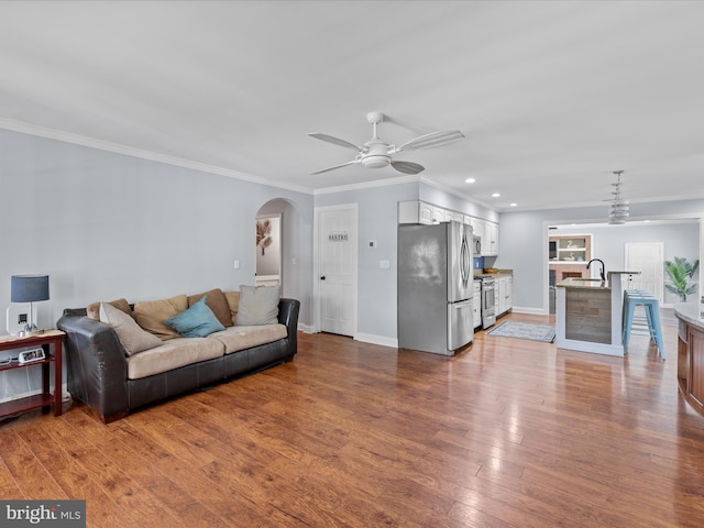 living room featuring crown molding, ceiling fan, arched walkways, dark wood finished floors, and recessed lighting