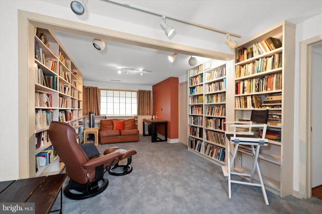 living area with wall of books, rail lighting, and carpet