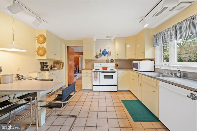 kitchen with light tile patterned floors, cream cabinets, a sink, track lighting, and white appliances