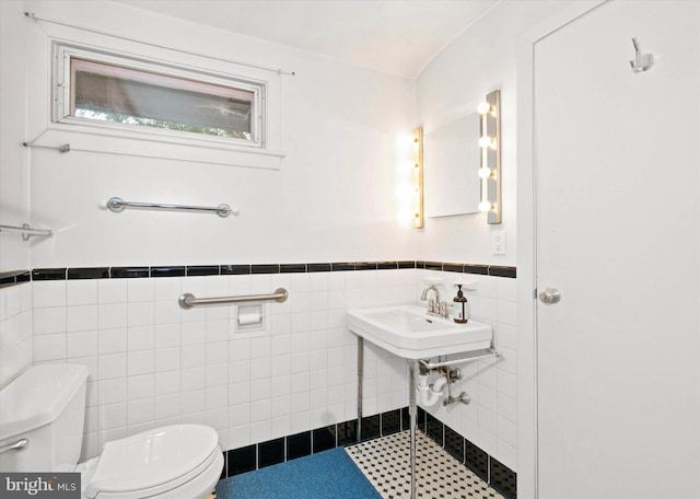 bathroom featuring a wainscoted wall, toilet, a sink, and tile walls