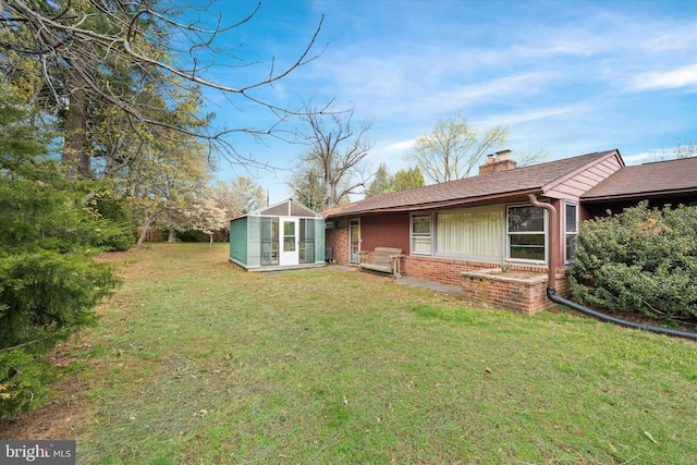 back of house with brick siding, an outdoor structure, a chimney, and a lawn