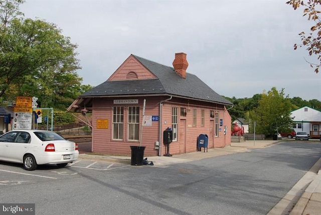 view of front facade featuring uncovered parking, a chimney, and a shingled roof