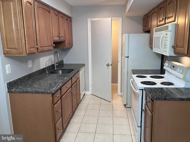 kitchen with white appliances, a sink, light tile patterned floors, dark stone countertops, and brown cabinetry
