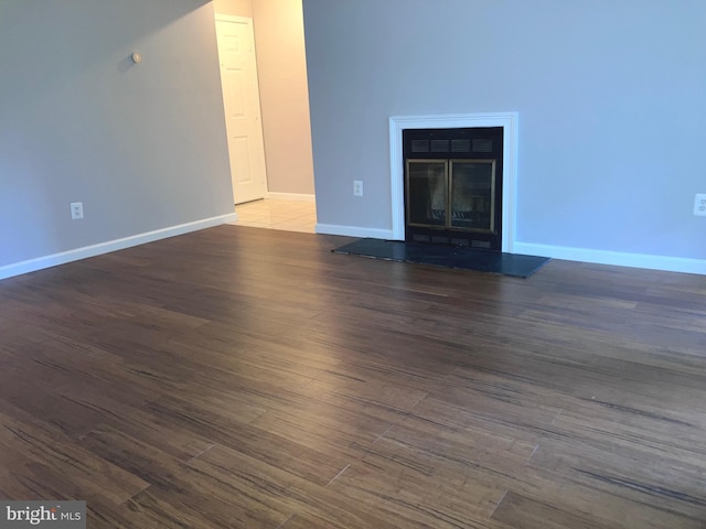 unfurnished living room featuring wood finished floors, baseboards, and a glass covered fireplace