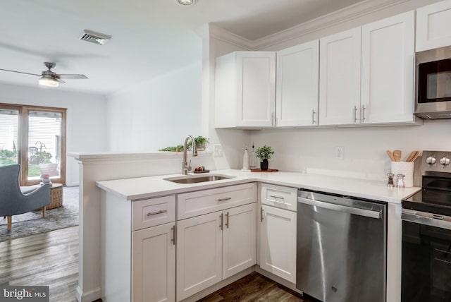 kitchen with a sink, white cabinets, a peninsula, appliances with stainless steel finishes, and dark wood-type flooring