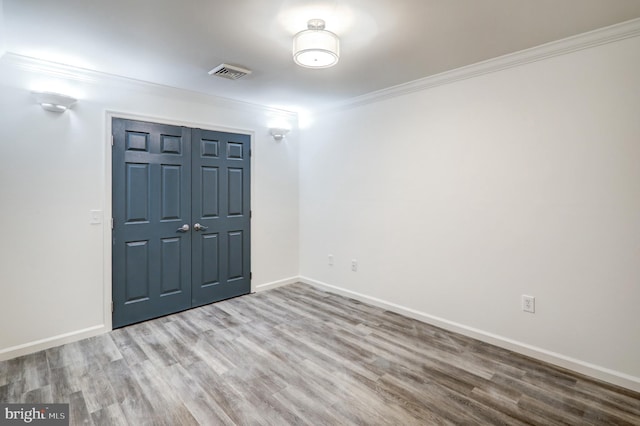 spare room featuring baseboards, wood finished floors, visible vents, and crown molding