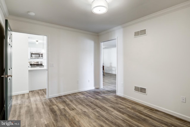 spare room with visible vents, baseboards, wood finished floors, and ornamental molding