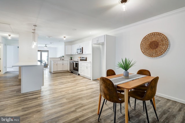 dining area featuring light wood finished floors, attic access, baseboards, a ceiling fan, and ornamental molding