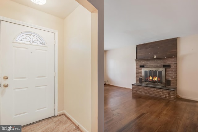 foyer featuring baseboards, a brick fireplace, and light wood-style flooring