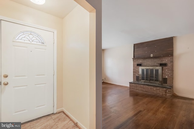 entrance foyer featuring light wood-style flooring, a brick fireplace, and baseboards