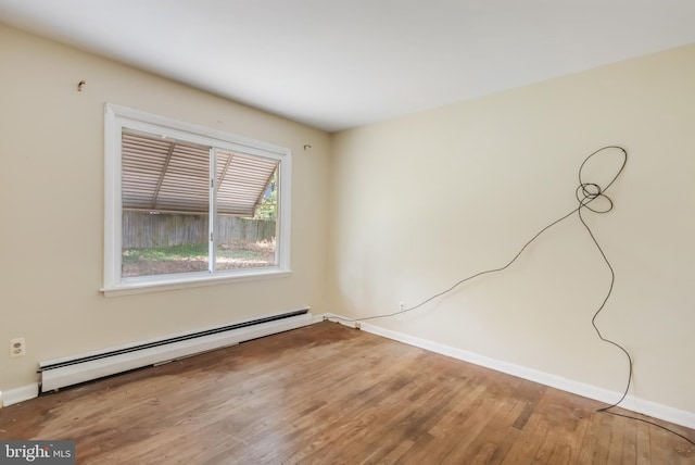 empty room with a baseboard heating unit, wood finished floors, and baseboards