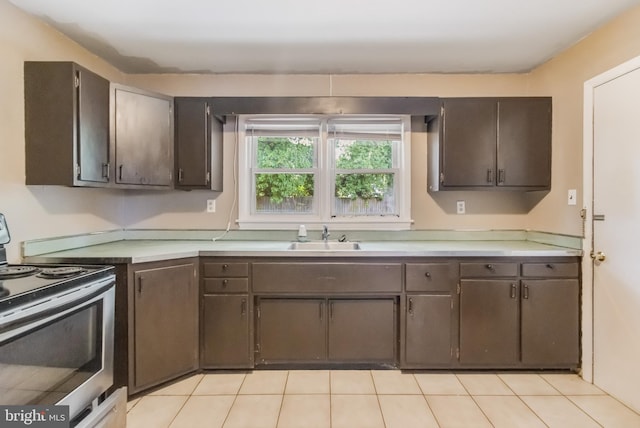 kitchen with dark brown cabinets, a sink, stainless steel range with electric cooktop, light tile patterned flooring, and light countertops