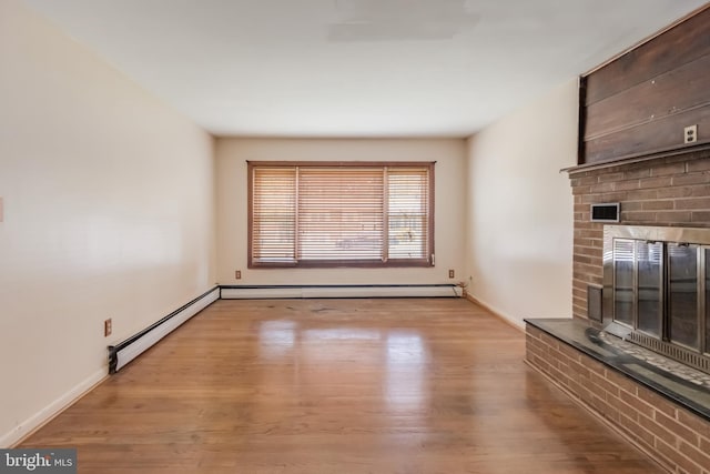 unfurnished living room with baseboard heating, baseboards, wood finished floors, and a fireplace