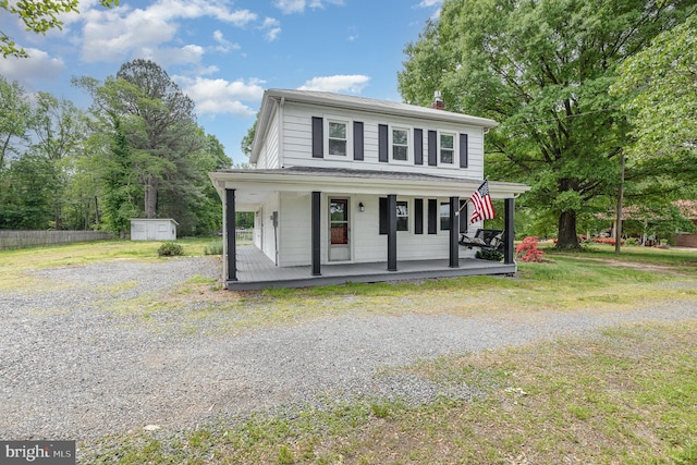 farmhouse with covered porch, a chimney, an outdoor structure, gravel driveway, and a storage unit