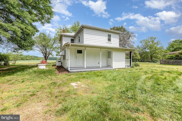 rear view of house with a lawn, fence, covered porch, and a chimney