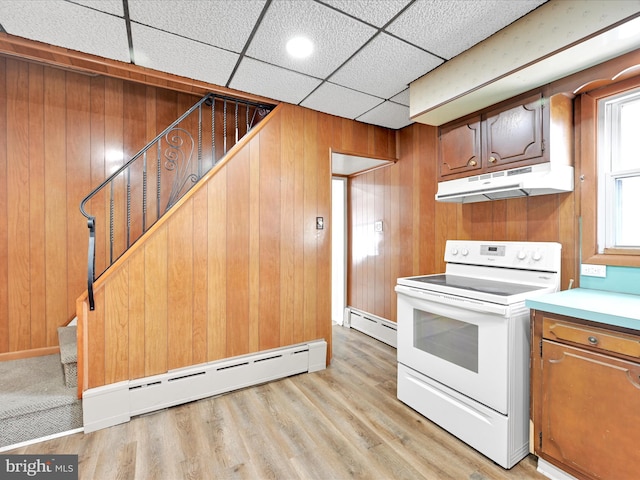 kitchen featuring white electric range oven, a baseboard radiator, wood walls, and under cabinet range hood