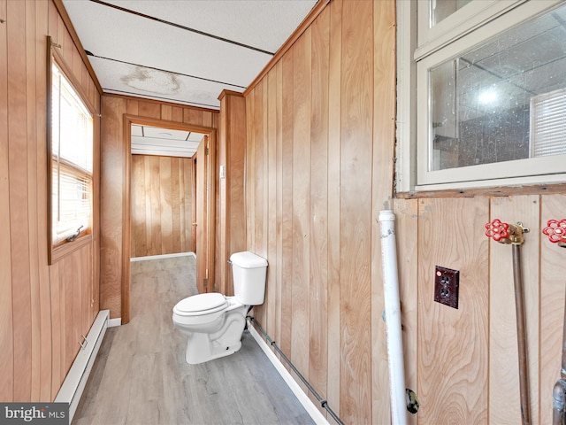 bathroom with a baseboard heating unit, wooden walls, wood finished floors, and toilet