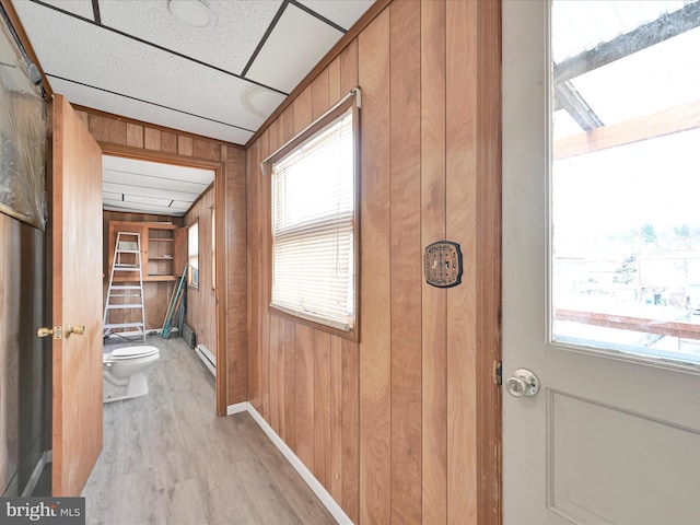 hall with light wood finished floors, wooden walls, and baseboards