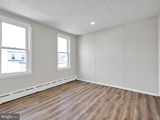 spare room with a baseboard heating unit, plenty of natural light, and wood finished floors