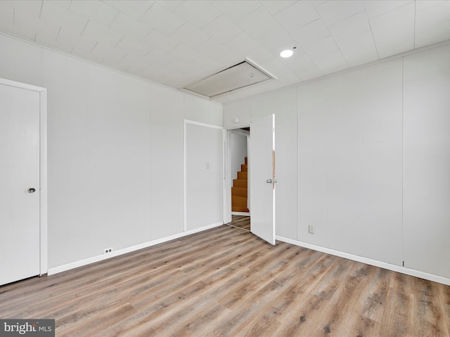 unfurnished room featuring attic access, wood finished floors, and baseboards