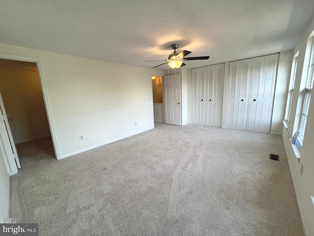 unfurnished bedroom with visible vents, a ceiling fan, light carpet, baseboards, and two closets