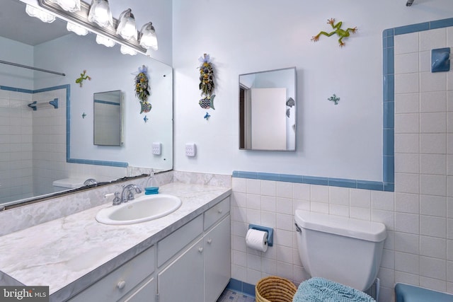 bathroom with a wainscoted wall, toilet, vanity, tile walls, and walk in shower