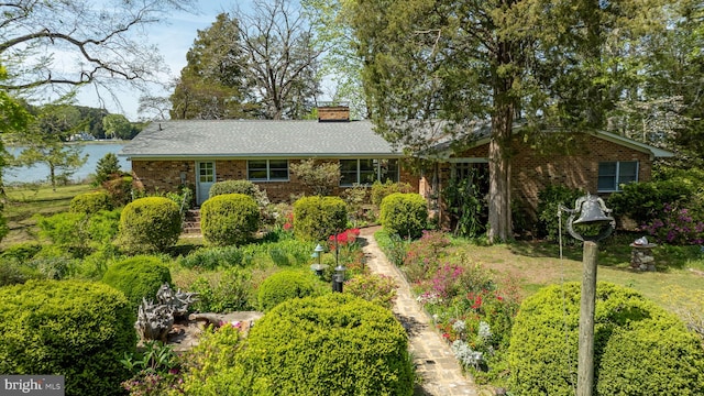 ranch-style house featuring brick siding, a chimney, and a water view