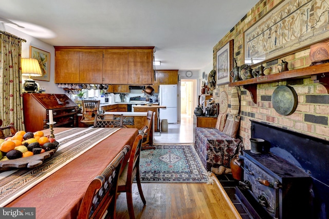 kitchen featuring electric range, freestanding refrigerator, wood finished floors, brown cabinetry, and light countertops