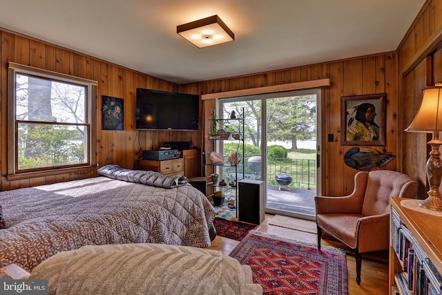 bedroom featuring wooden walls, wood finished floors, access to outside, and multiple windows