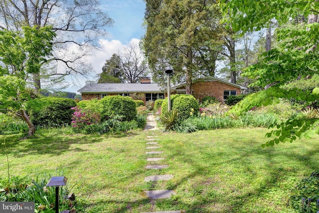 single story home with a chimney, brick siding, and a front yard