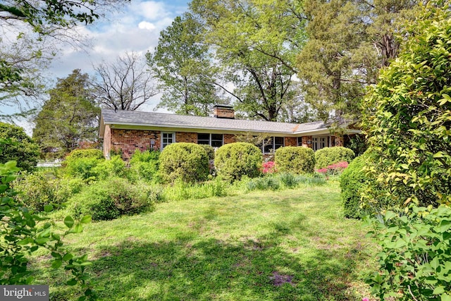 exterior space featuring brick siding, a front yard, and a chimney