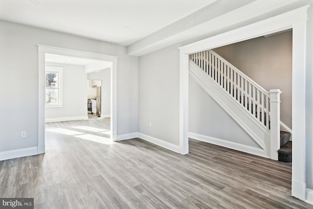 unfurnished living room featuring baseboards, stairway, and wood finished floors