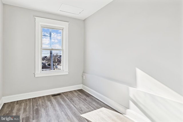 unfurnished room with attic access, visible vents, wood finished floors, and baseboards