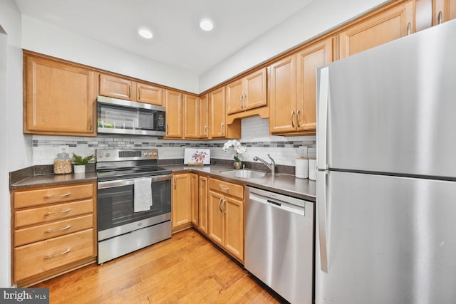 kitchen featuring dark countertops, stainless steel appliances, light wood finished floors, and a sink