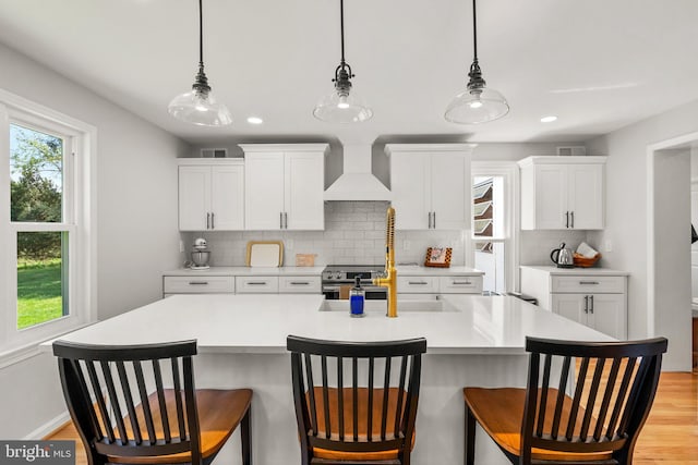 kitchen with visible vents, a kitchen bar, backsplash, light countertops, and premium range hood