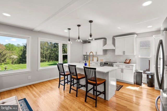 kitchen featuring an island with sink, stainless steel appliances, light countertops, wall chimney exhaust hood, and decorative backsplash