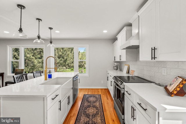 kitchen featuring light countertops, backsplash, a sink, light wood-style flooring, and appliances with stainless steel finishes