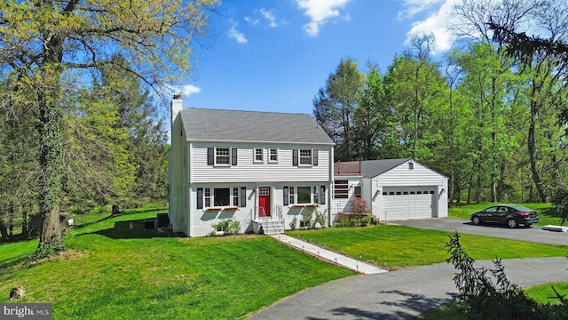 colonial inspired home featuring a front lawn, driveway, a chimney, entry steps, and an attached garage