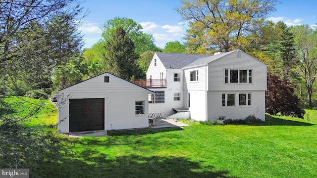 rear view of property with a garage, a yard, an outbuilding, and a balcony