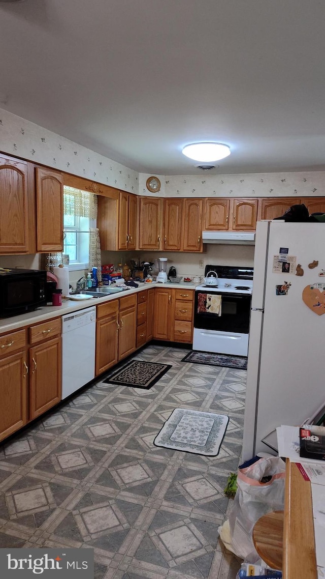 kitchen with a sink, white appliances, light floors, light countertops, and under cabinet range hood