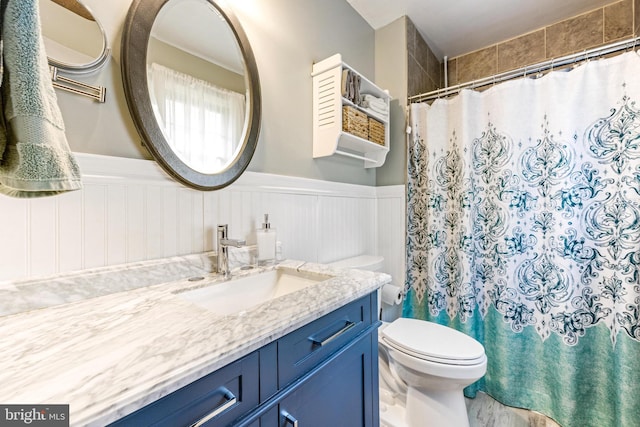 bathroom with vanity, toilet, a shower with shower curtain, and wainscoting