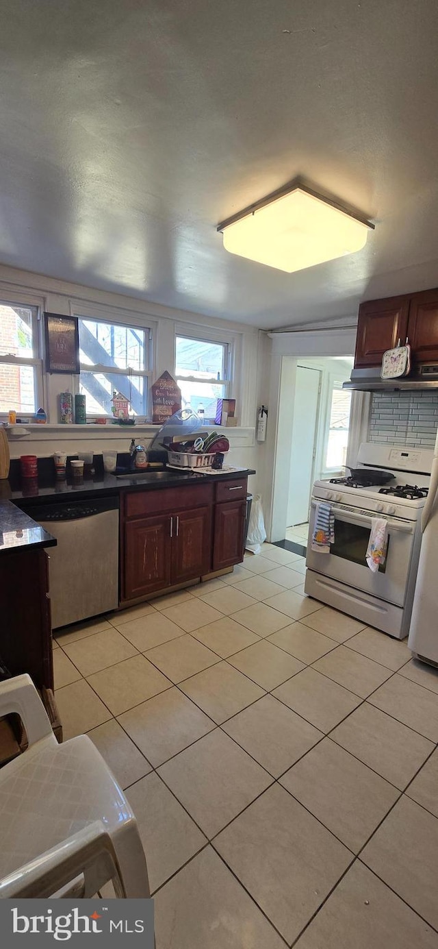 kitchen featuring light tile patterned floors, white gas range oven, stainless steel dishwasher, and plenty of natural light