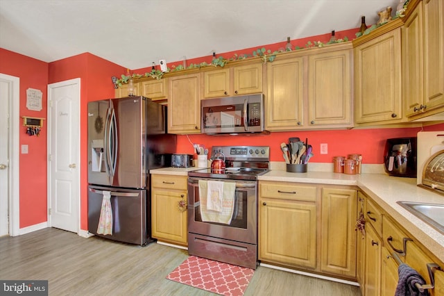 kitchen with light countertops, light wood-style flooring, appliances with stainless steel finishes, and baseboards