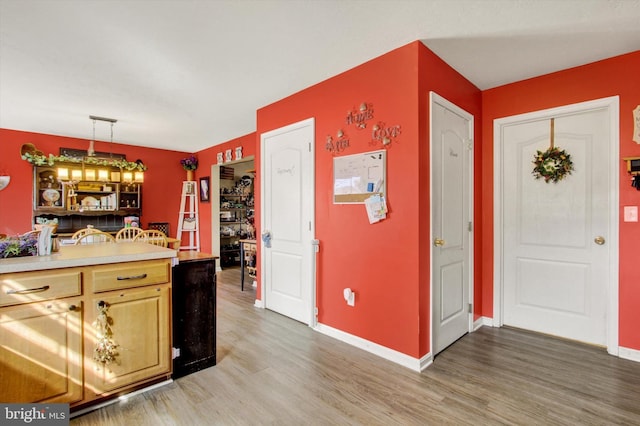 kitchen featuring baseboards, hanging light fixtures, light countertops, and light wood-type flooring