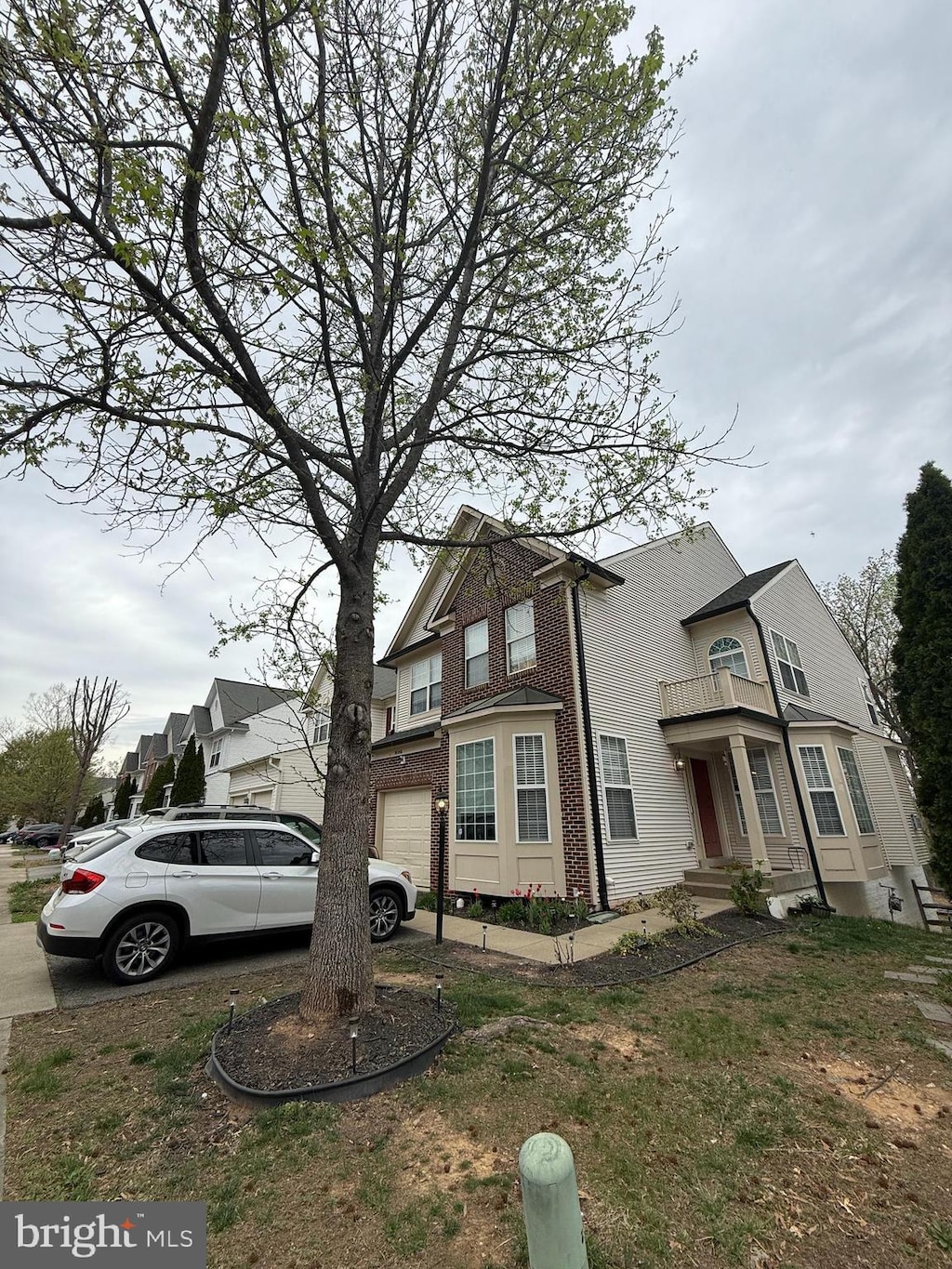 view of front facade with a balcony, an attached garage, driveway, and brick siding