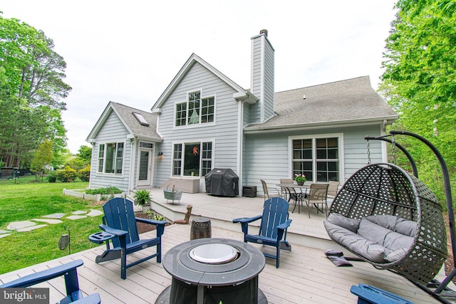 rear view of house featuring a chimney, roof with shingles, a lawn, a wooden deck, and outdoor dining space